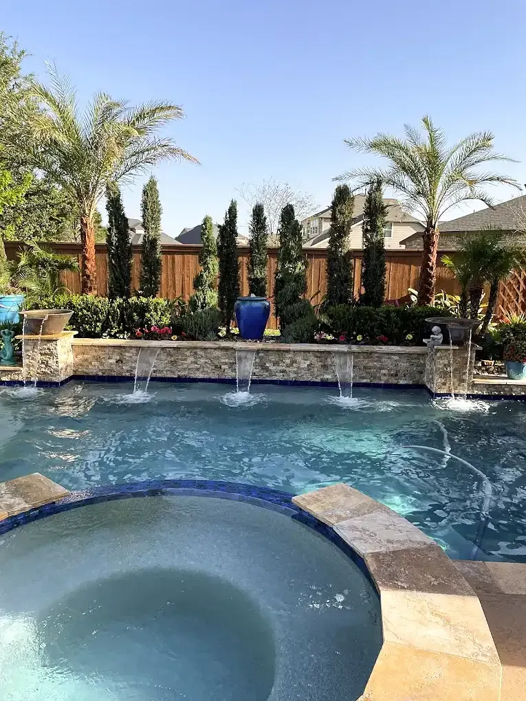Pool with fountains, hot tub, and lush landscaping on a sunny day.