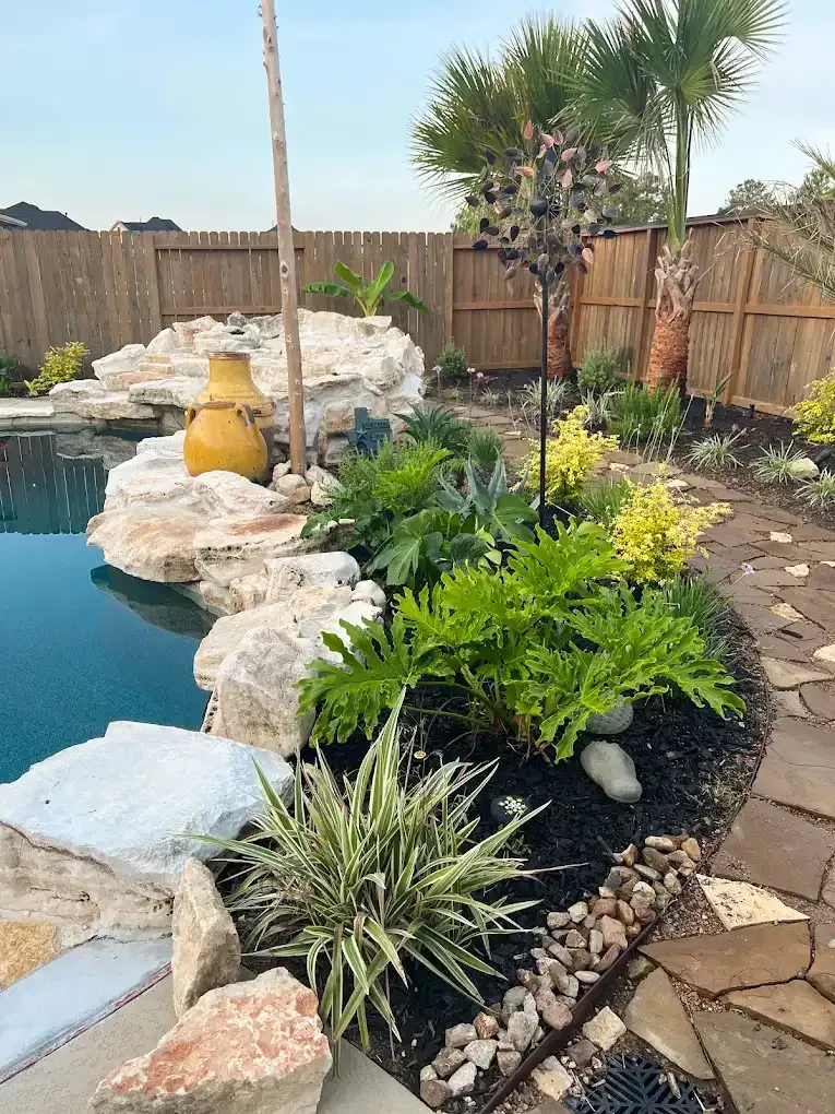 Poolside landscaping with rocks, lush plants, and a yellow vase.