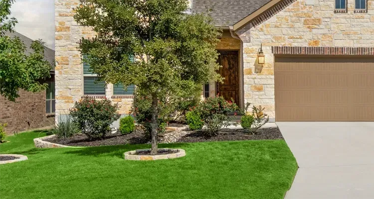 House exterior with stone facade, lush green lawn, tree, and tan garage door.