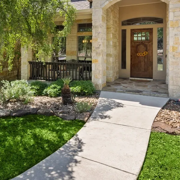 A concrete walkway curves towards a home's entryway. Lush grass and plants line the path.