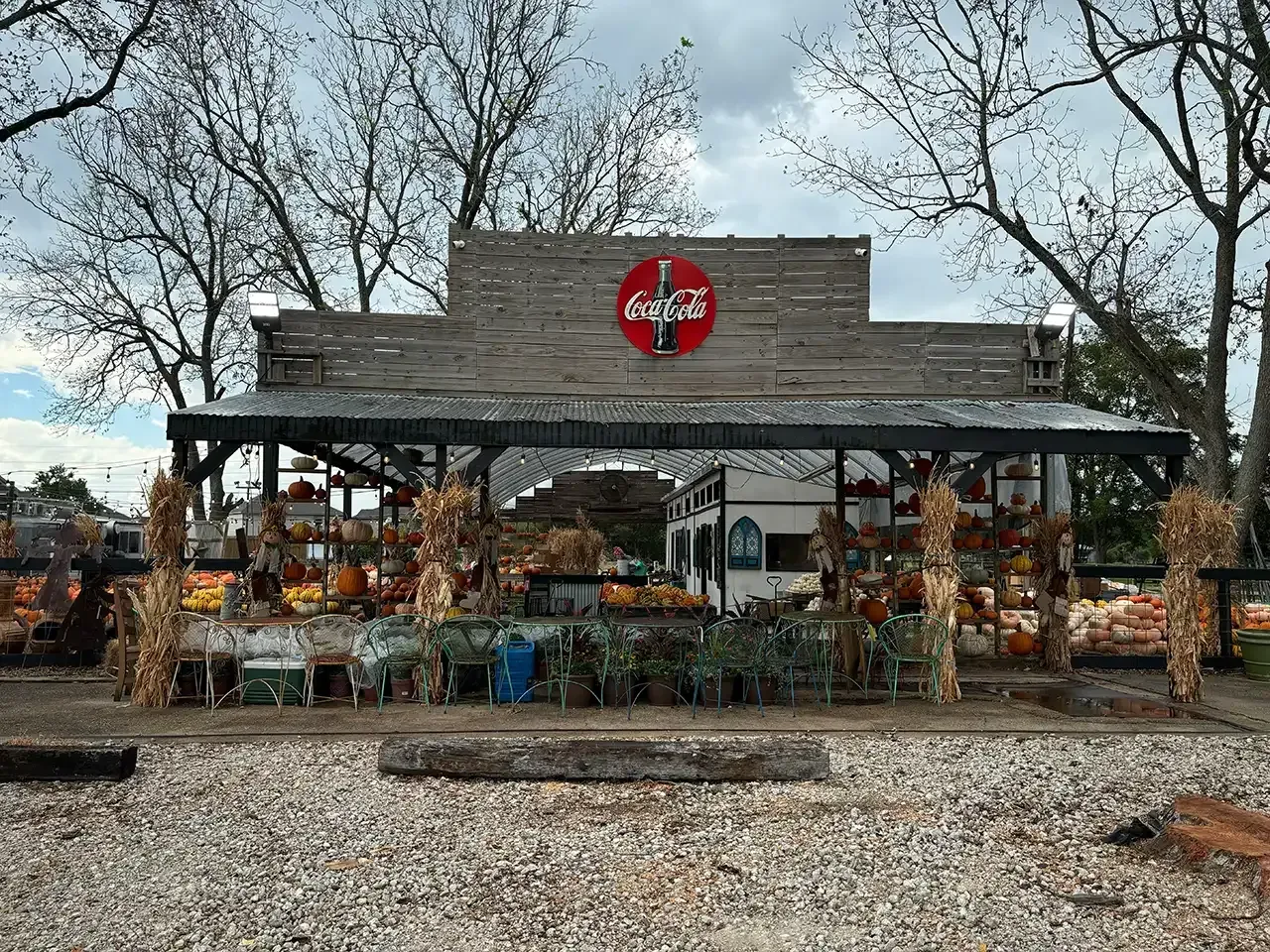 Wooden farm stand with Coca-Cola sign, decorated for fall with pumpkins and corn stalks.