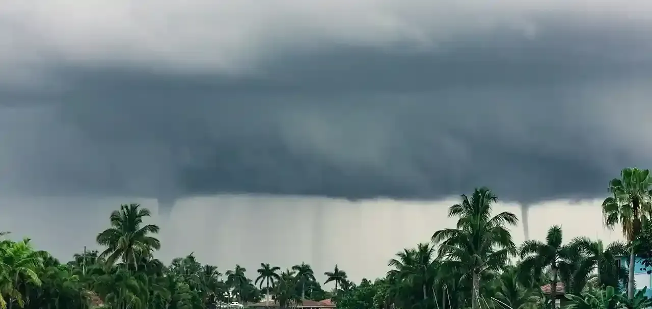 Dark, stormy clouds above a tropical landscape with two funnel clouds reaching down.