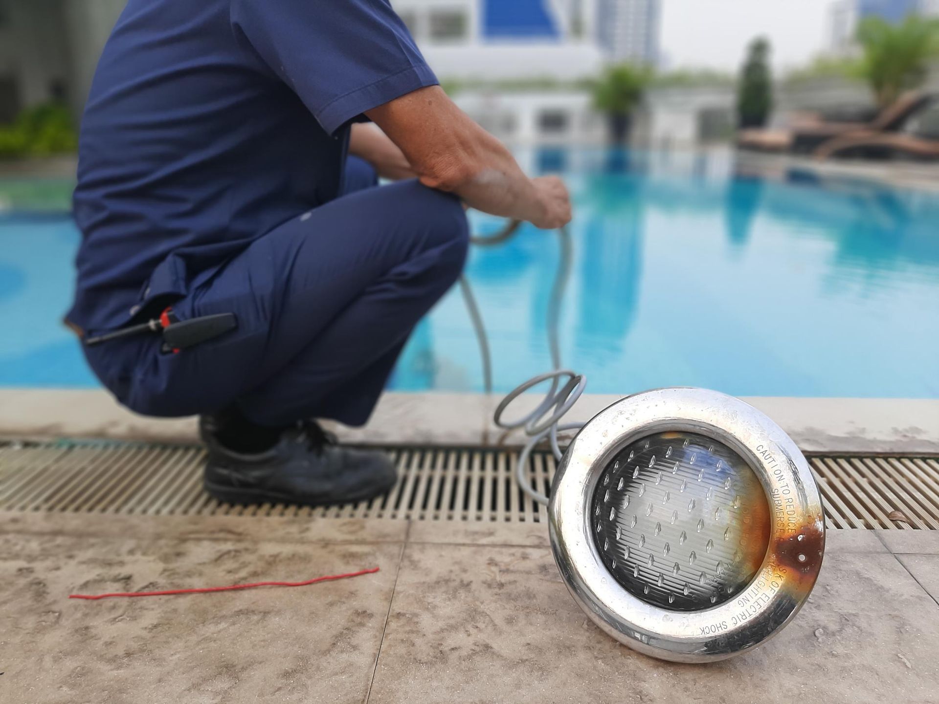 Pool technician kneeling near pool, replacing underwater light fixture.