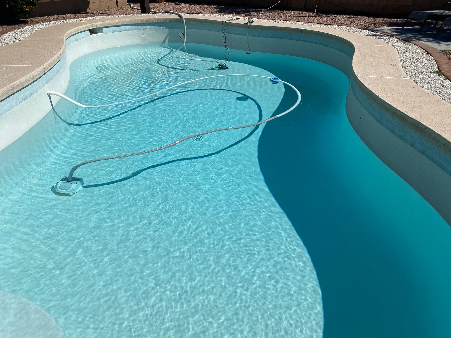 A swimming pool with clear turquoise water and a white vacuum hose.  The pool has a light-colored concrete edge.