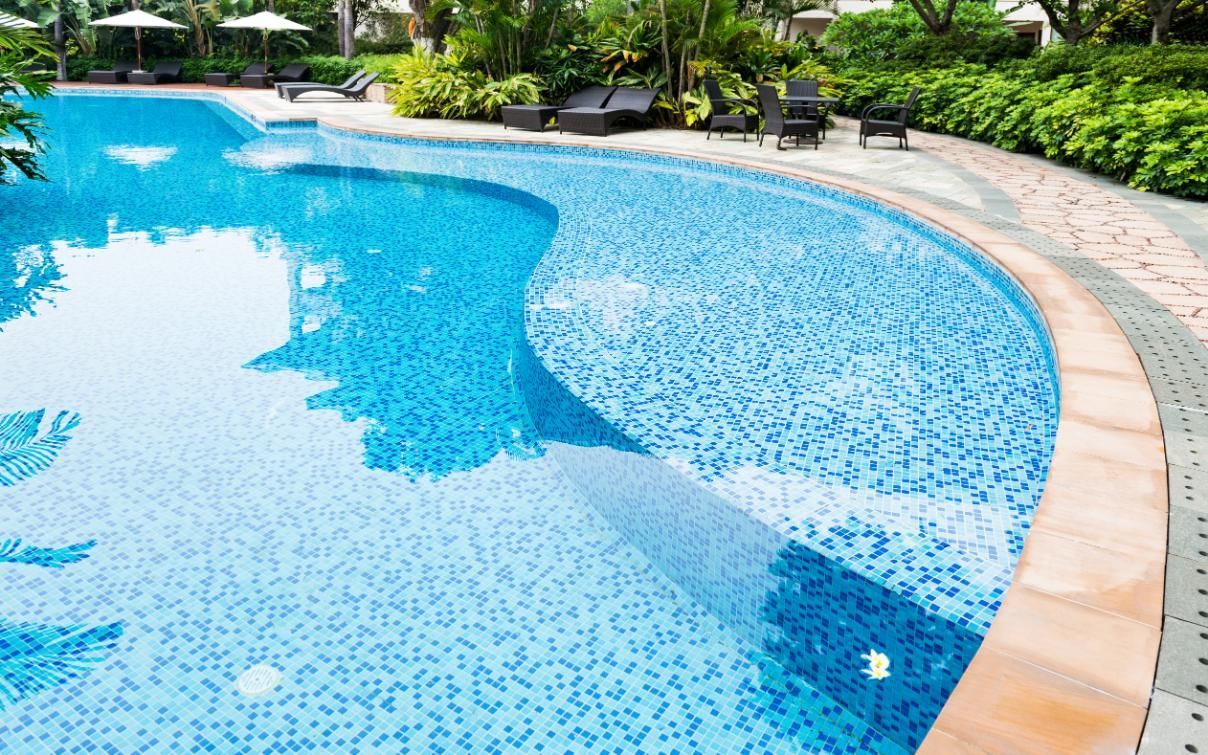 Blue-tiled swimming pool with curved edges, surrounded by a paved walkway and lush greenery.