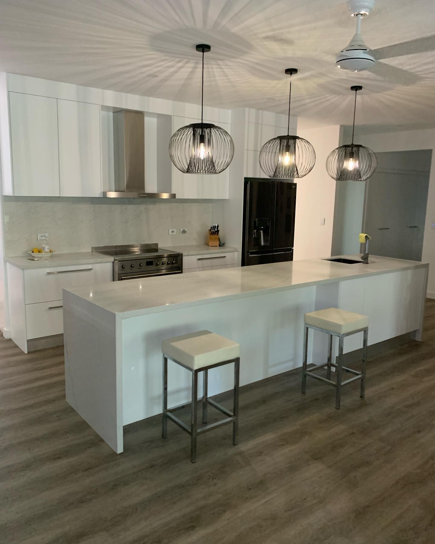 A Stylish Kitchen Featuring White Cabinets, Stools, a Refrigerator, and a Stove — Expert Cabinetmaker on the Sunshine Coast QLD