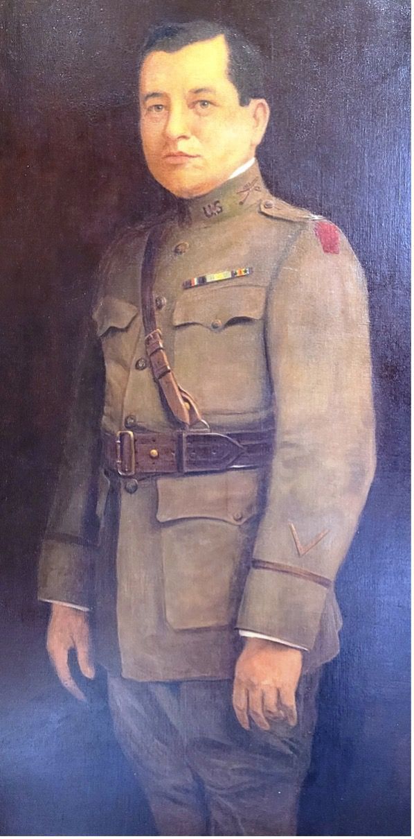 Portrait of a man in a military uniform. He has dark hair and is wearing a tan uniform with red epaulettes.