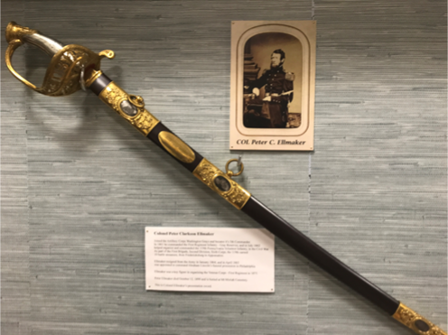 Naval officer's sword with ornate gold details and a black handle. A vintage photo of the officer is displayed alongside.