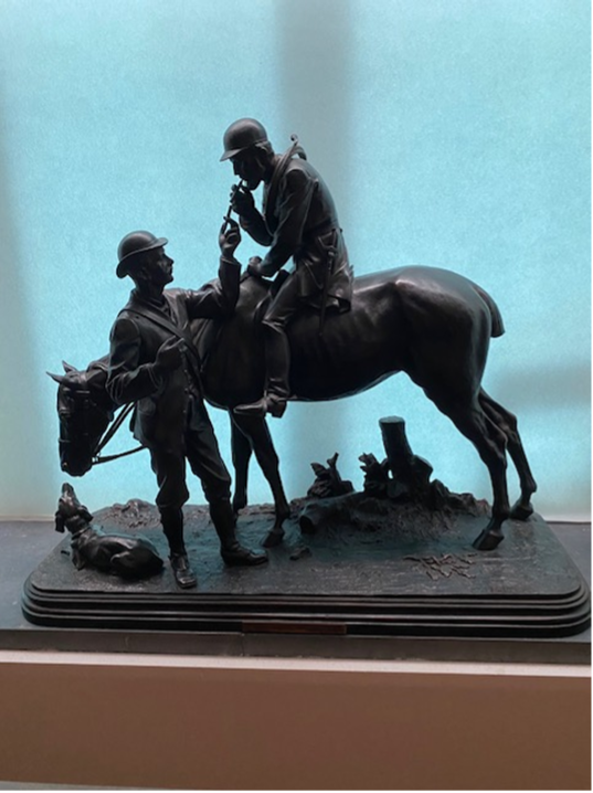 Bronze sculpture of two men, one on horseback, the other standing with a dog, in a field.
