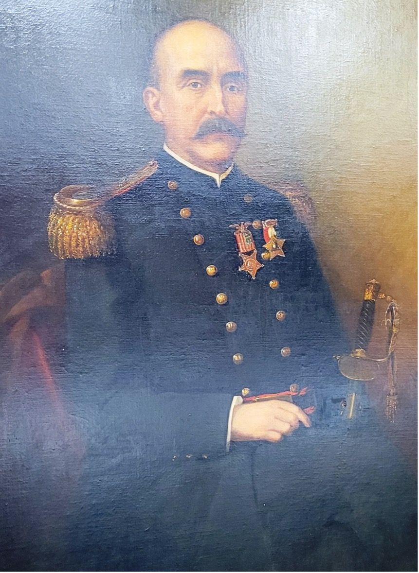 Portrait of a man in a dark blue naval uniform with gold epaulettes, medals, and a sword; he has a mustache.