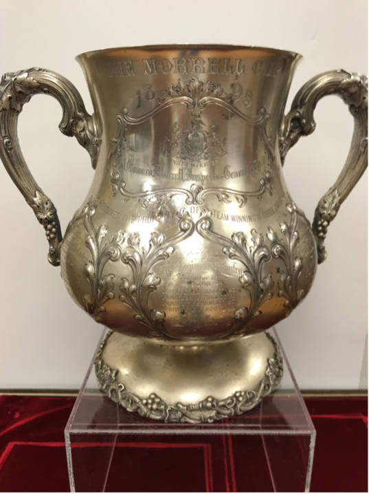 Silver trophy cup with ornate handles and floral designs, displayed on a red surface.