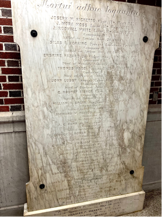 Marble memorial plaque with engraved names on a red brick wall background.
