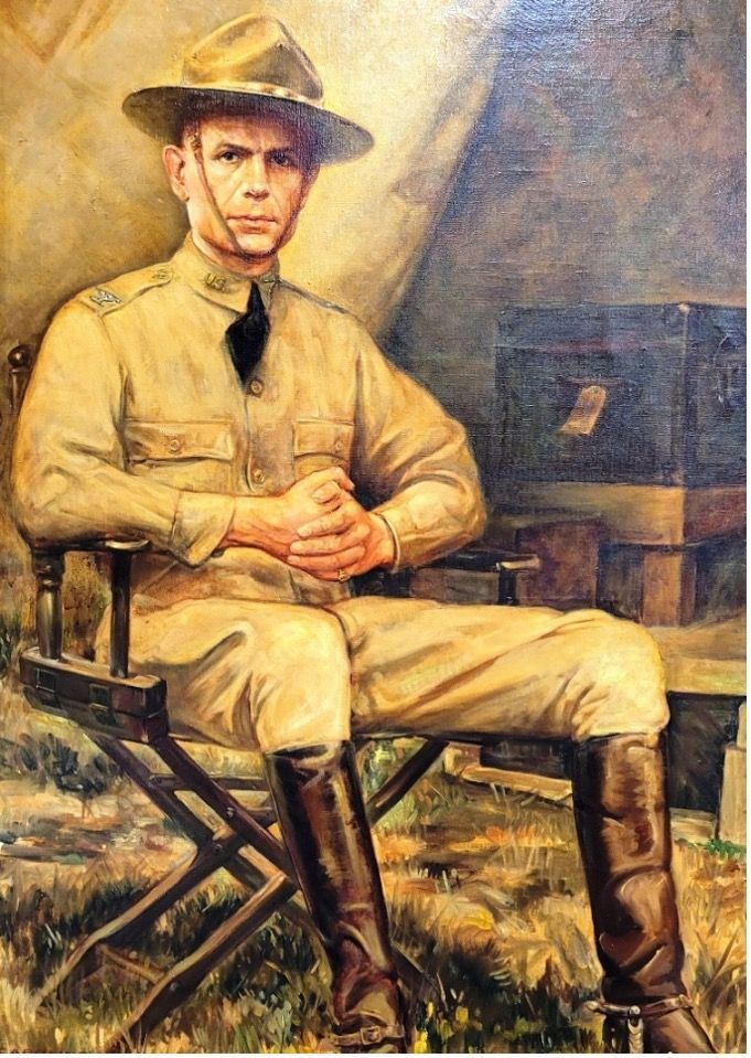 A seated man in military attire, wearing a hat, boots, and looking serious.
