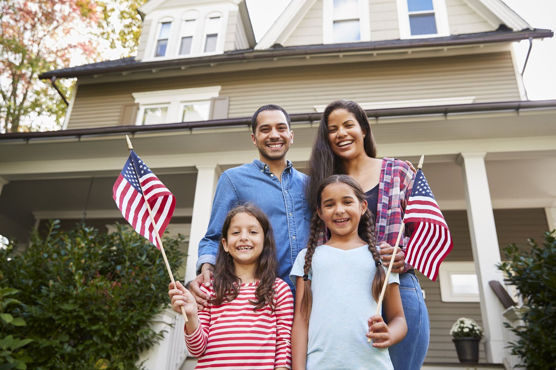 A family is standing in front of their house holding american flags.