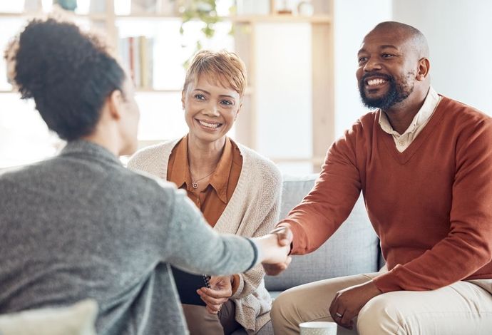 A man and a woman are shaking hands while sitting on a couch.