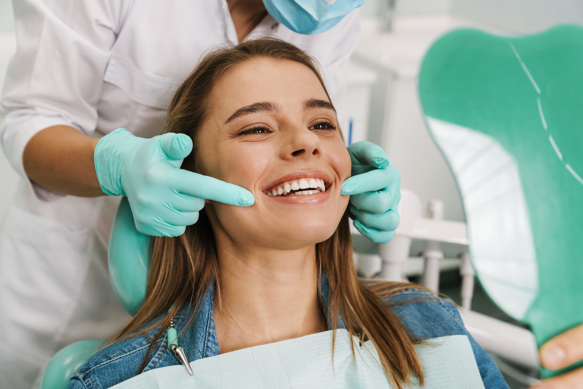 A woman is sitting in a dental chair while a dentist examines her teeth.