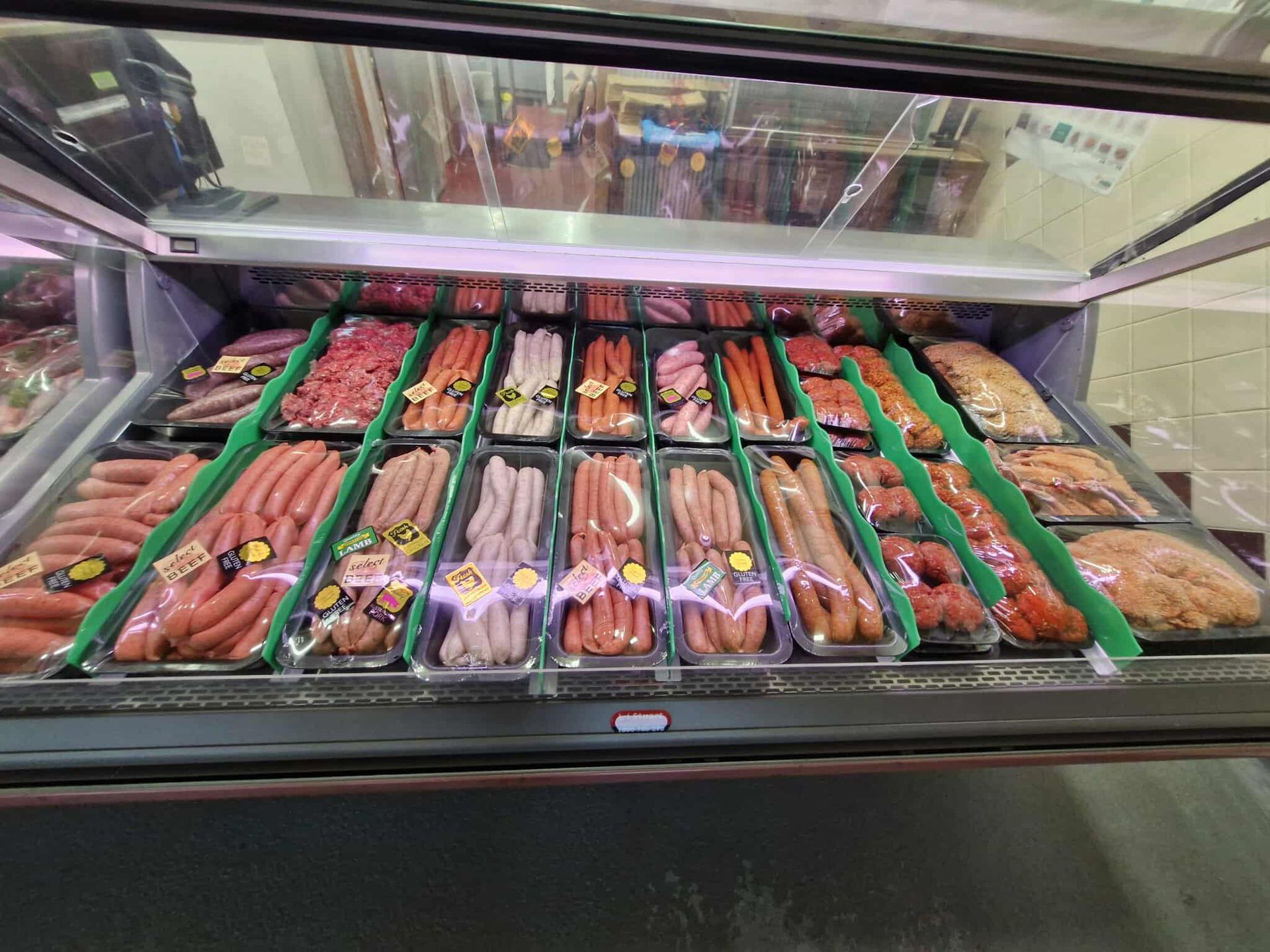 Meat display case in a grocery store, with various packaged sausages and raw meats.