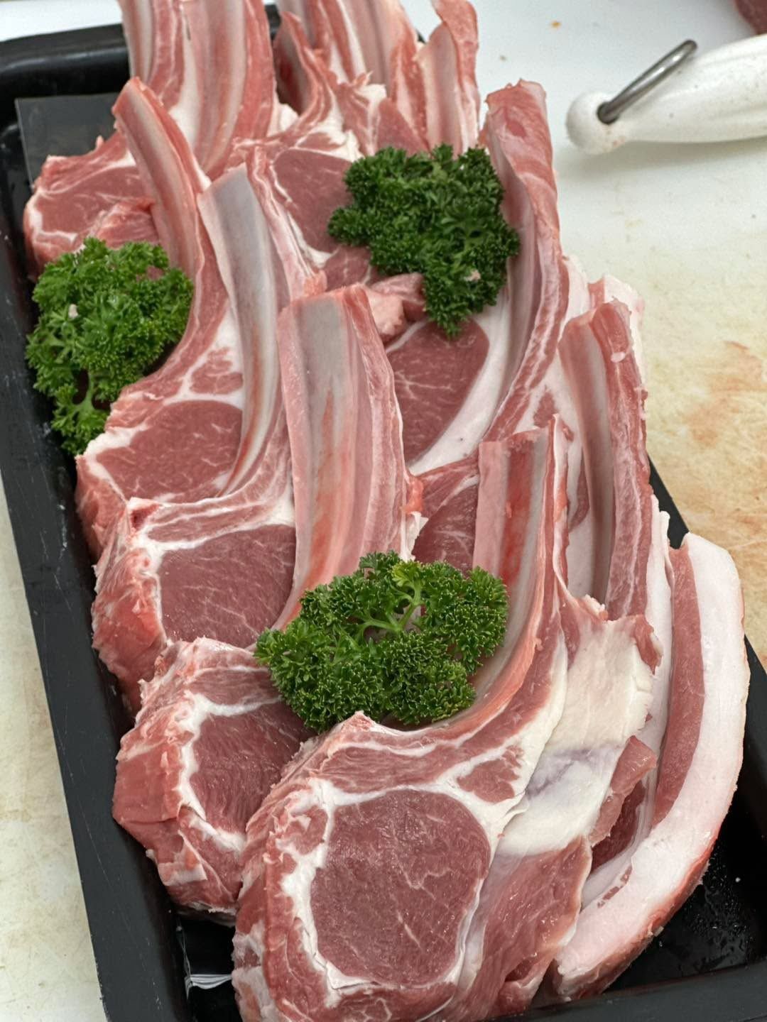 Rack of raw lamb chops in a black tray, garnished with green parsley.