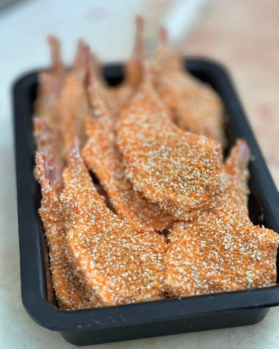Breaded lamb chops in a black tray, ready for cooking.