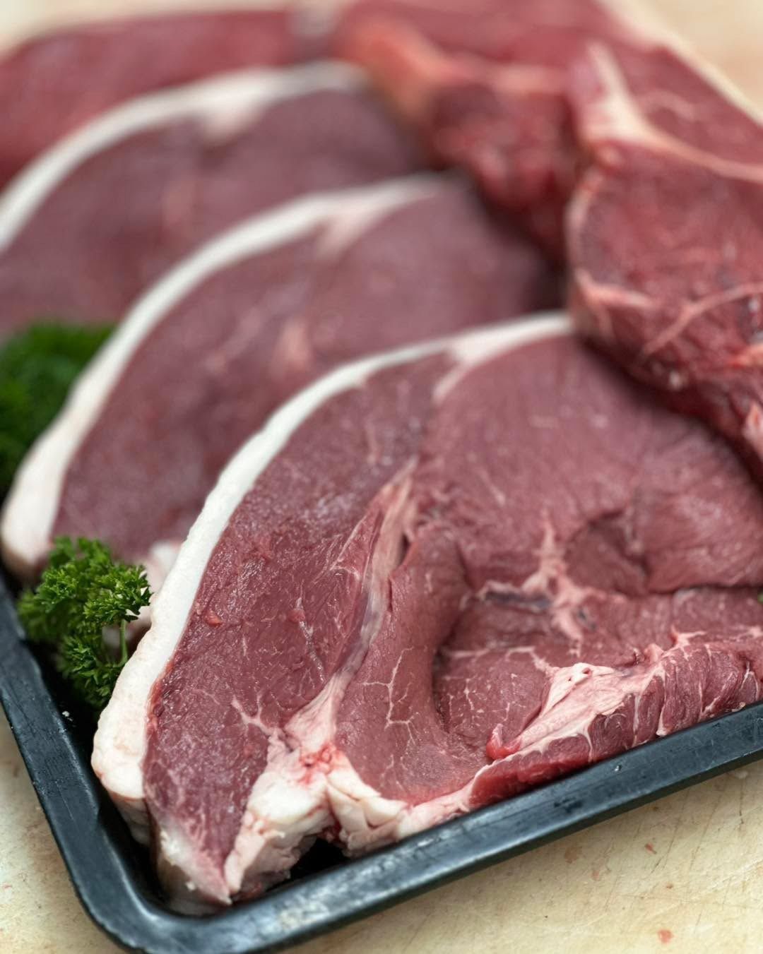 Raw, sliced beef steaks with fat marbling in a black tray.