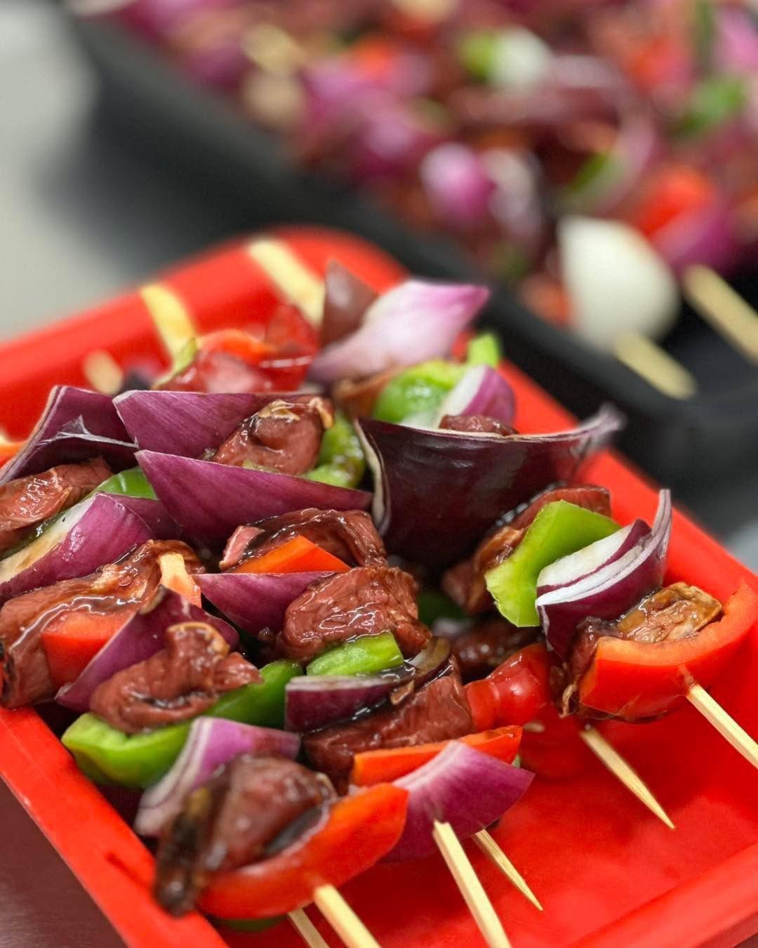 Skewers with sausage, red onion, bell peppers, on a red tray.