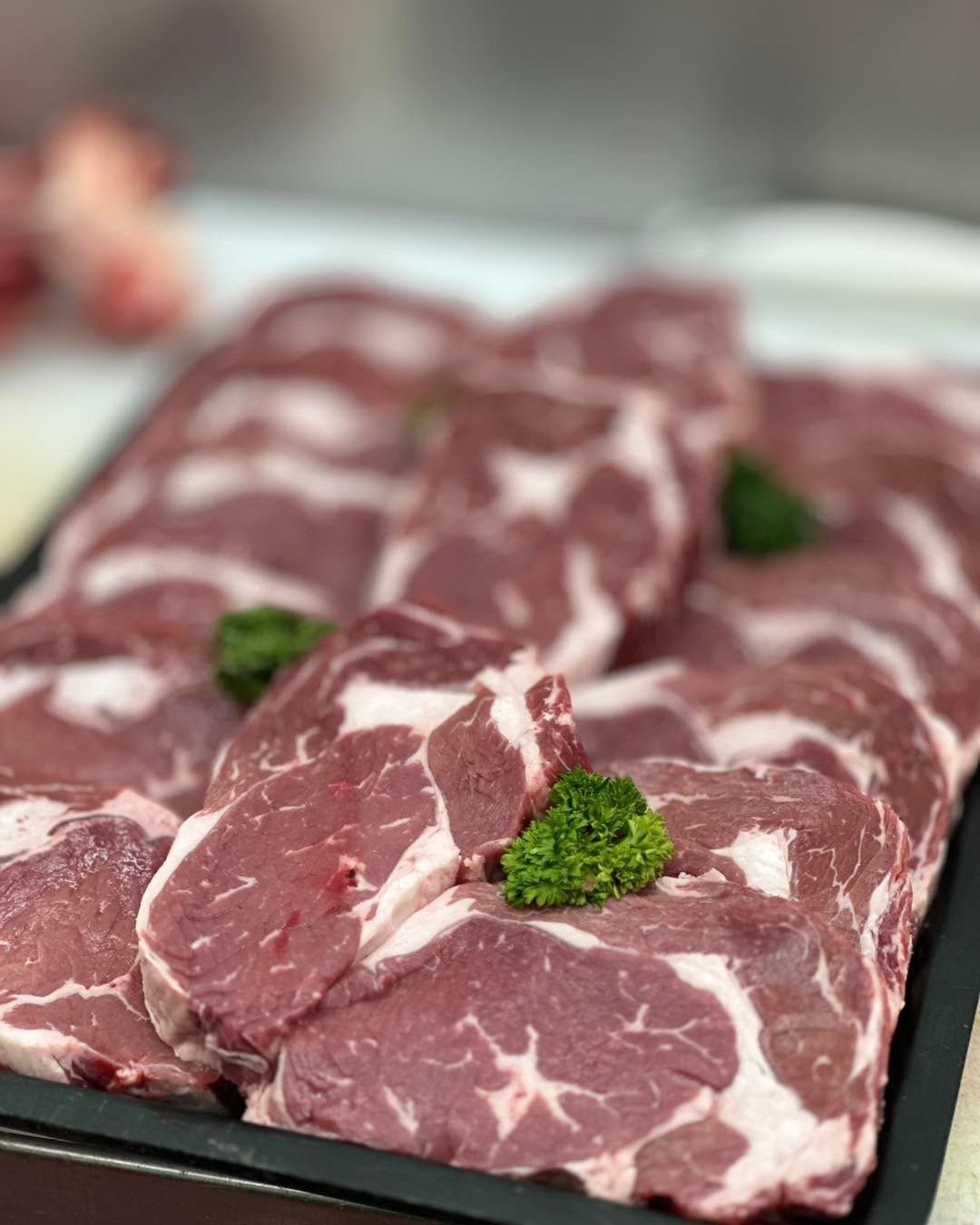 Raw meat steaks with visible marbling, arranged on a black tray, garnished with parsley.