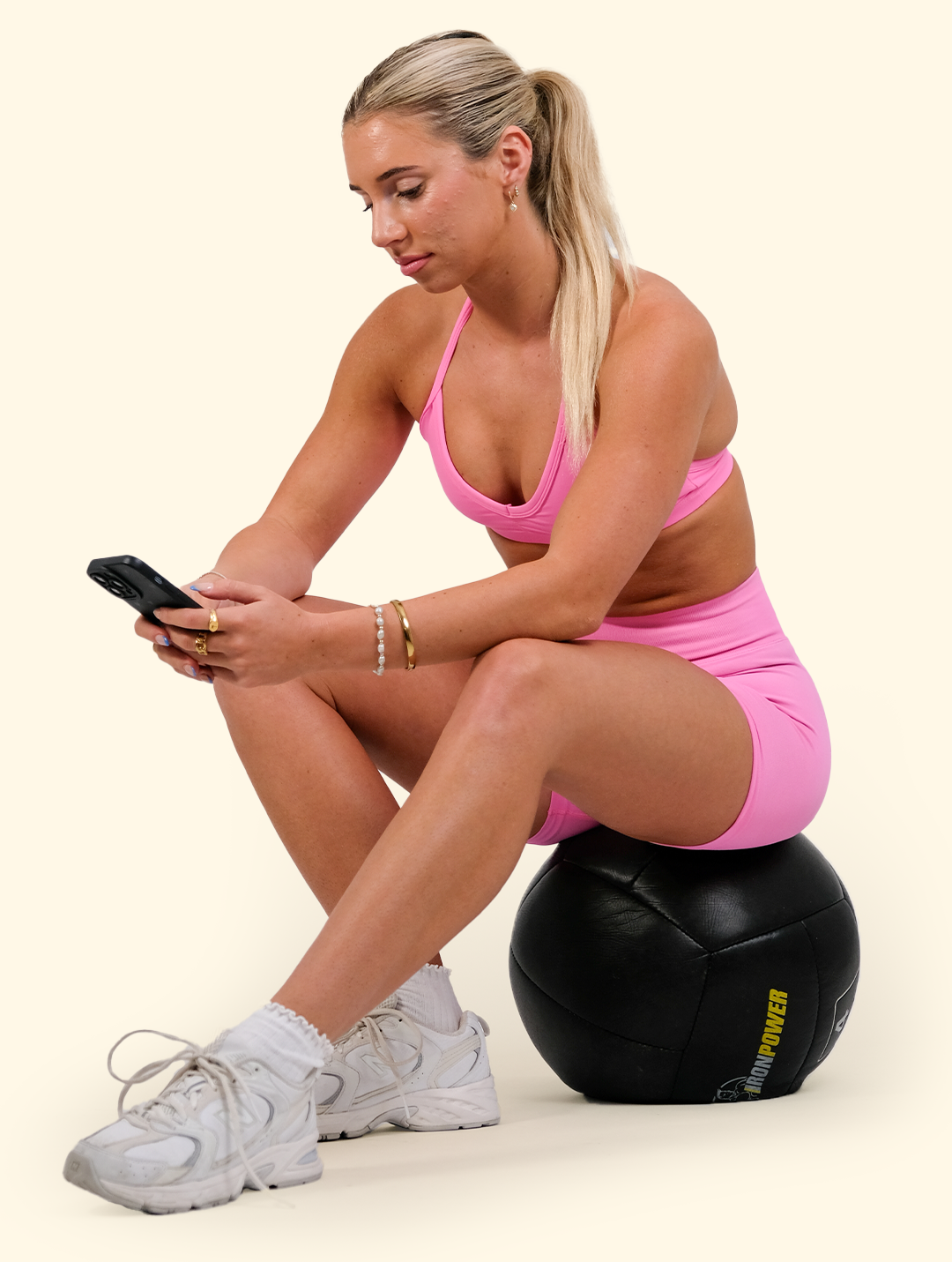 A woman is sitting on a medicine ball looking at her phone.