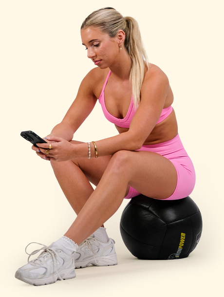 A woman is sitting on a ball looking at her phone.