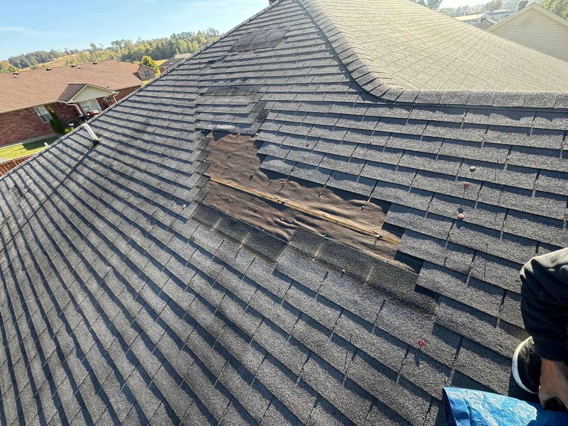 Damaged roof with missing shingles; sunlight on asphalt.