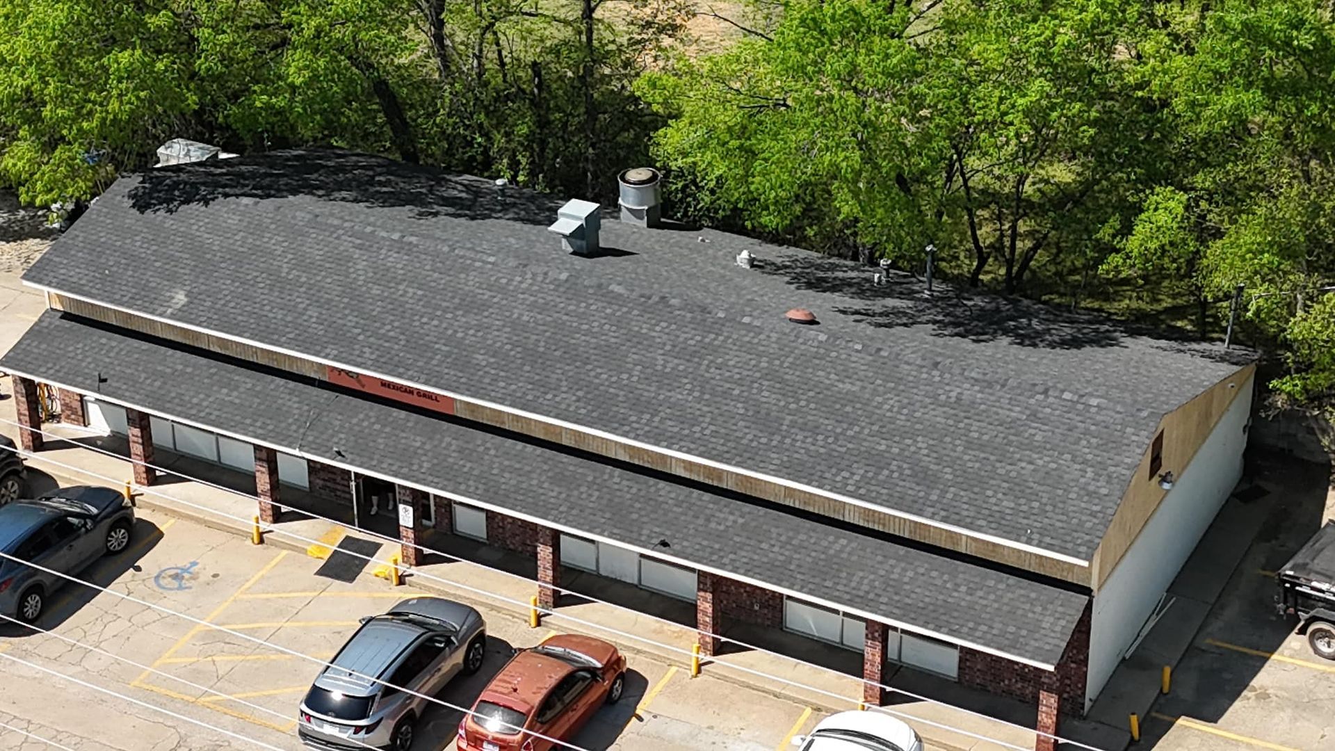 Long, low building with dark roof; several parked cars in front, trees in the background.
