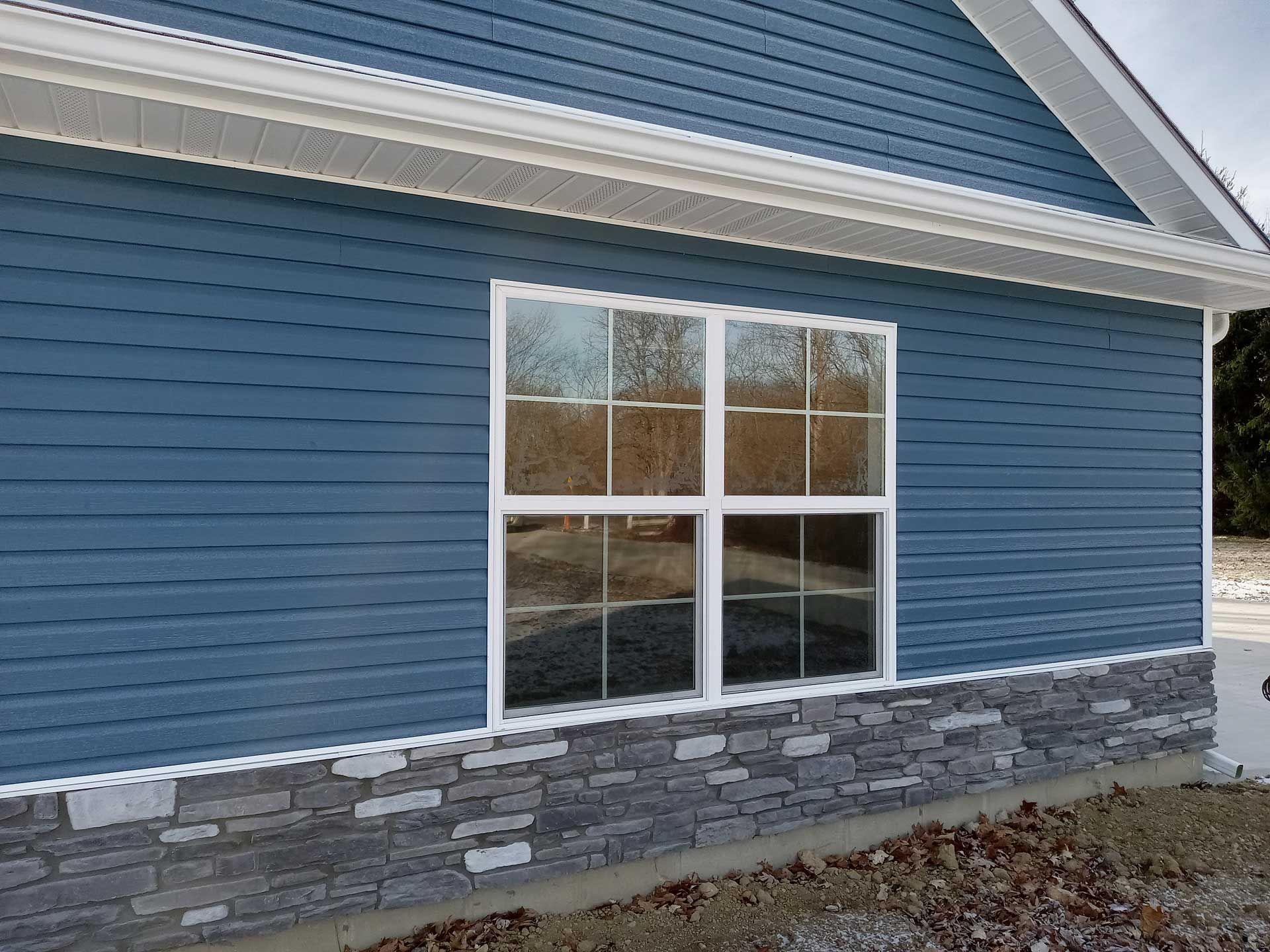 Blue siding house with white-framed window and stone veneer base, white trim.