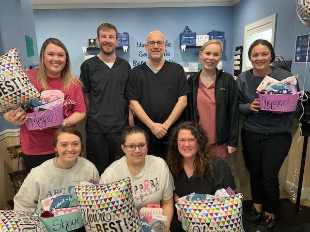 Group of dental office staff holding gifts, smiling. They are indoors, celebrating.