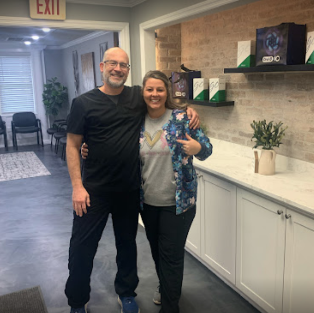 A man and a woman smiling, arms around each other, in a doctor's office.