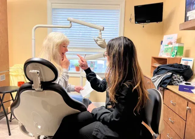 Woman in dentist chair, dentist pointing at paperwork, bright office setting.