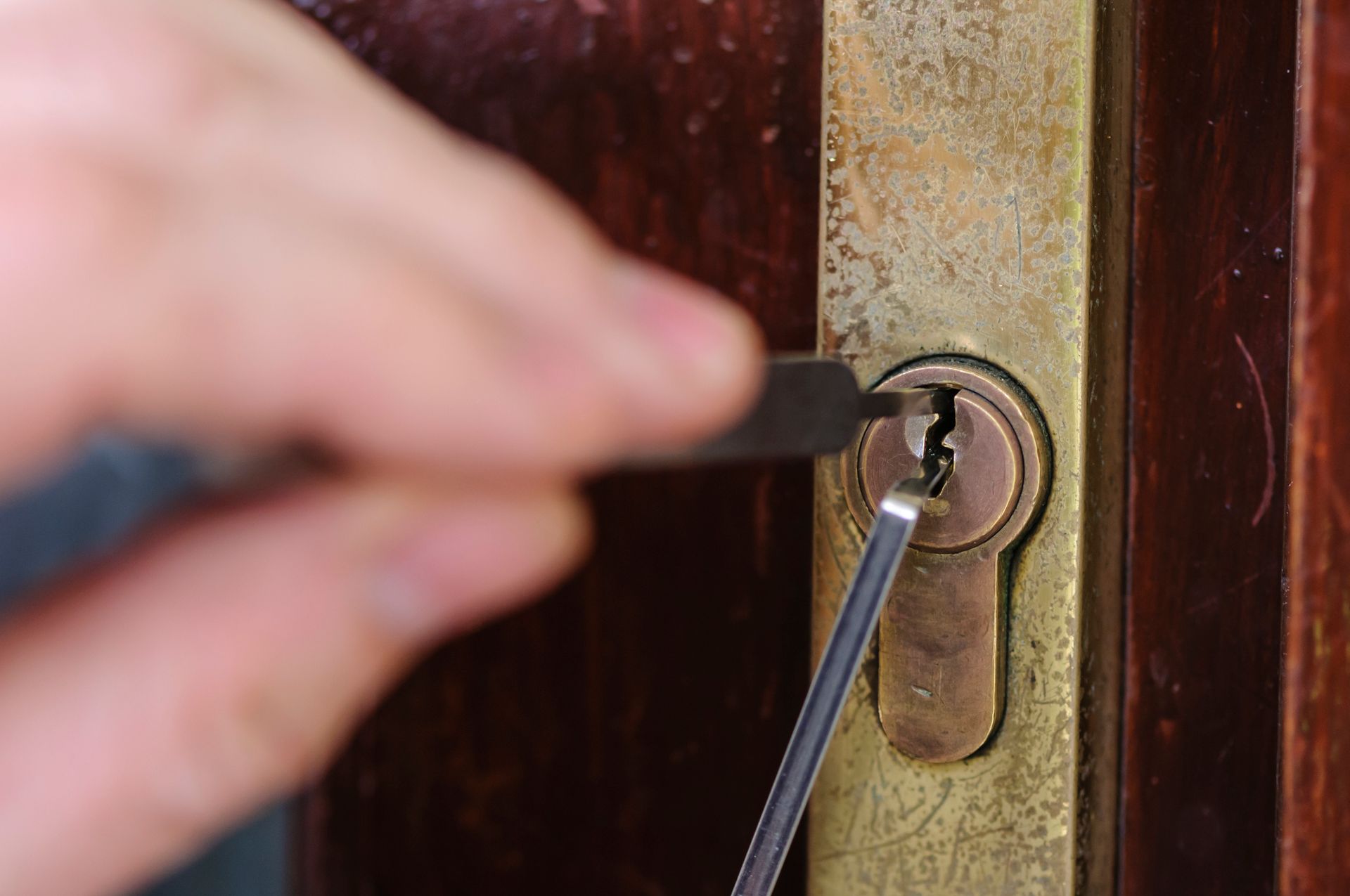 A person is using lock picks to open a brass door lock on a wooden door.