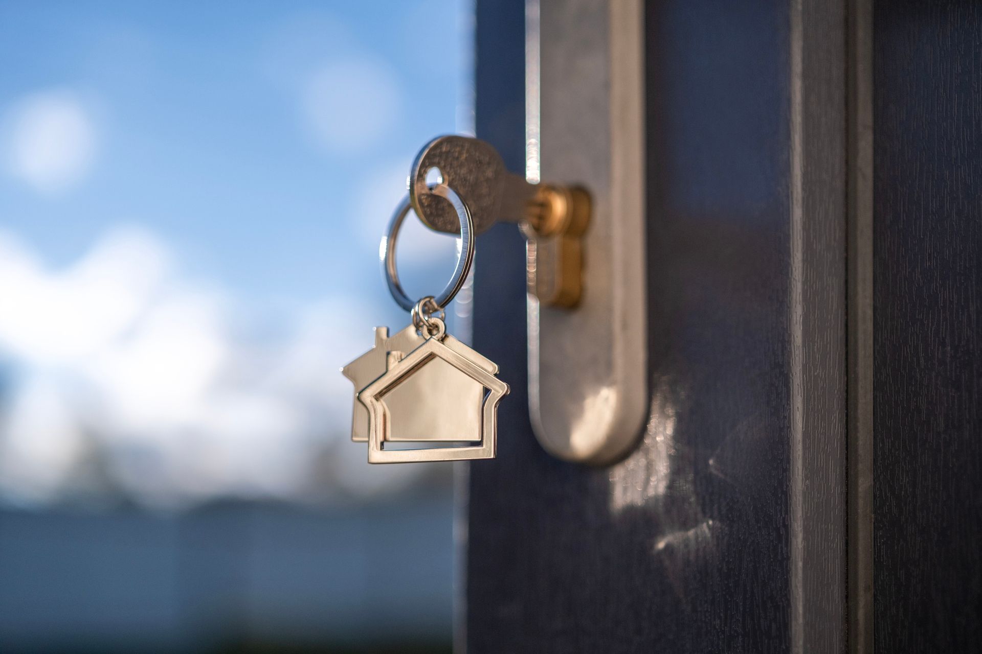 A close up of a key in a door lock with a keychain in the shape of a house.