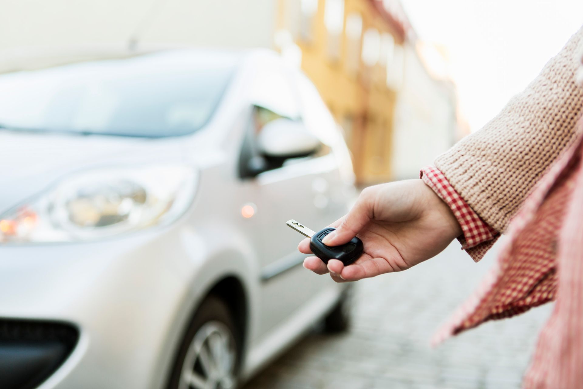 A woman is holding a car key in front of a car.