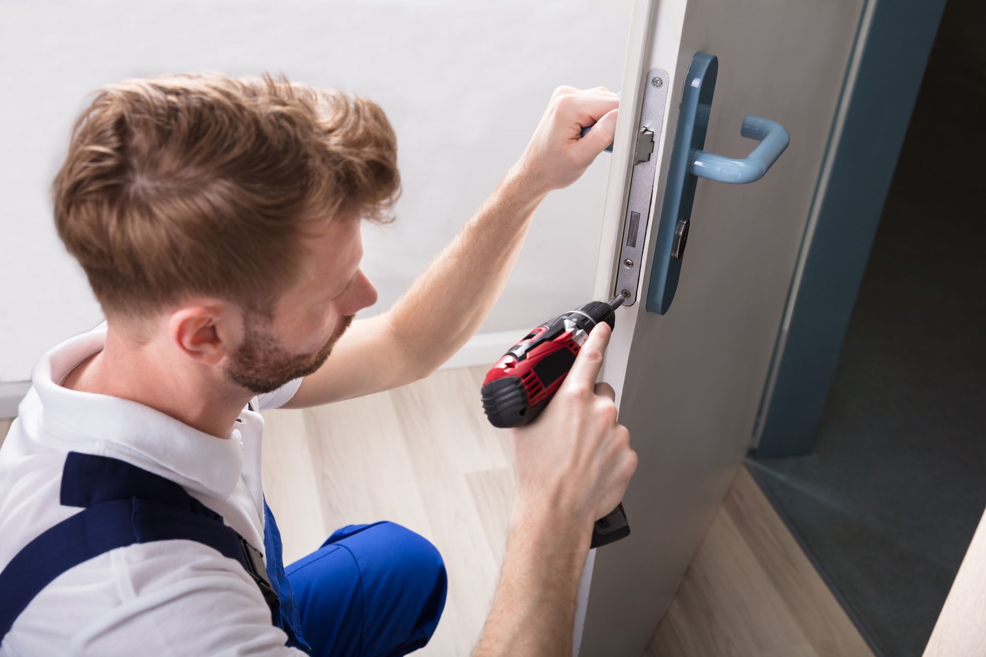 Locksmith using power drill to repair door lock mechanism during installation.
