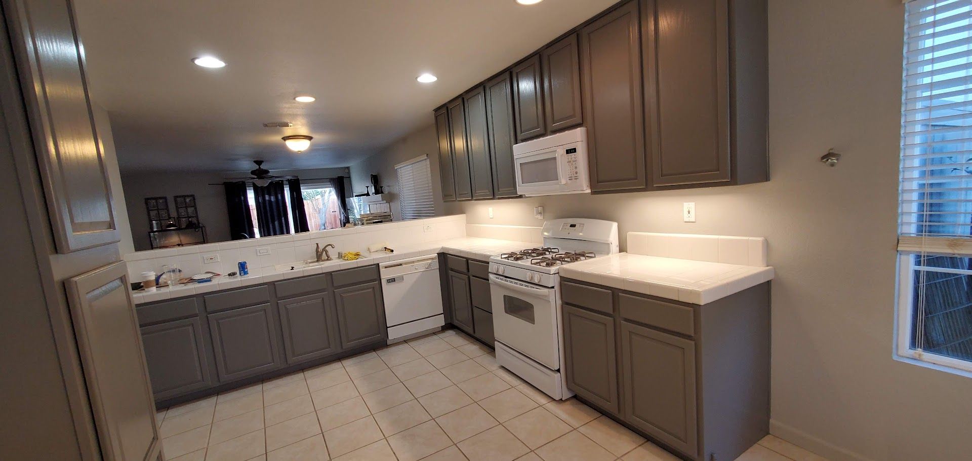 Kitchen with gray cabinets, white appliances, and a pass-through to a living area.
