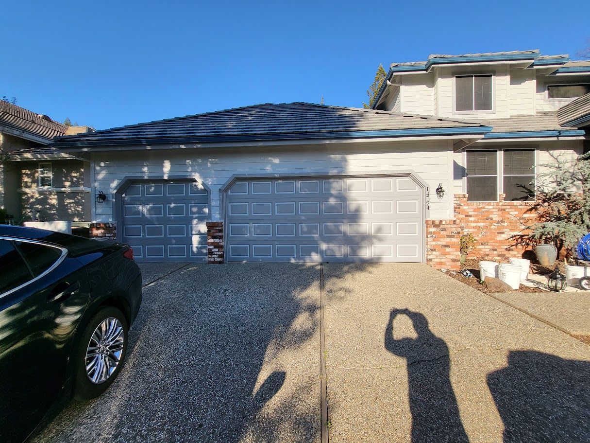 A house with a two-car garage, gravel driveway, and a dark green car parked on the left.