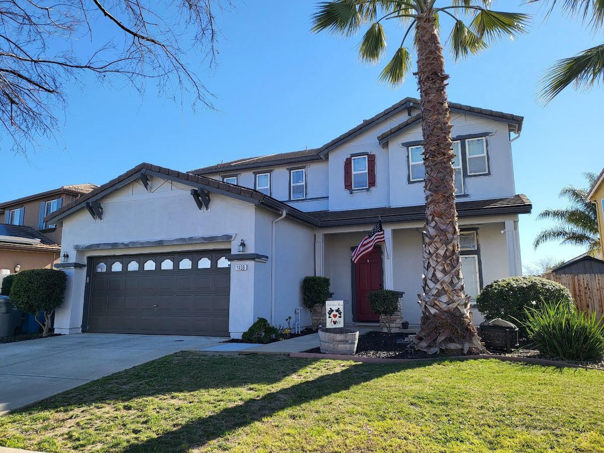 Two-story suburban house with gray exterior, brown garage door, and a palm tree in front.
