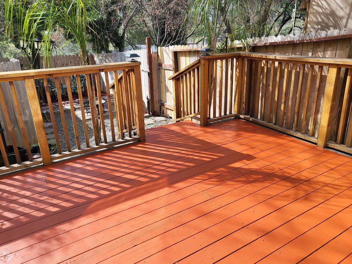 Wooden deck with orange stain and wooden railing; outdoor setting.