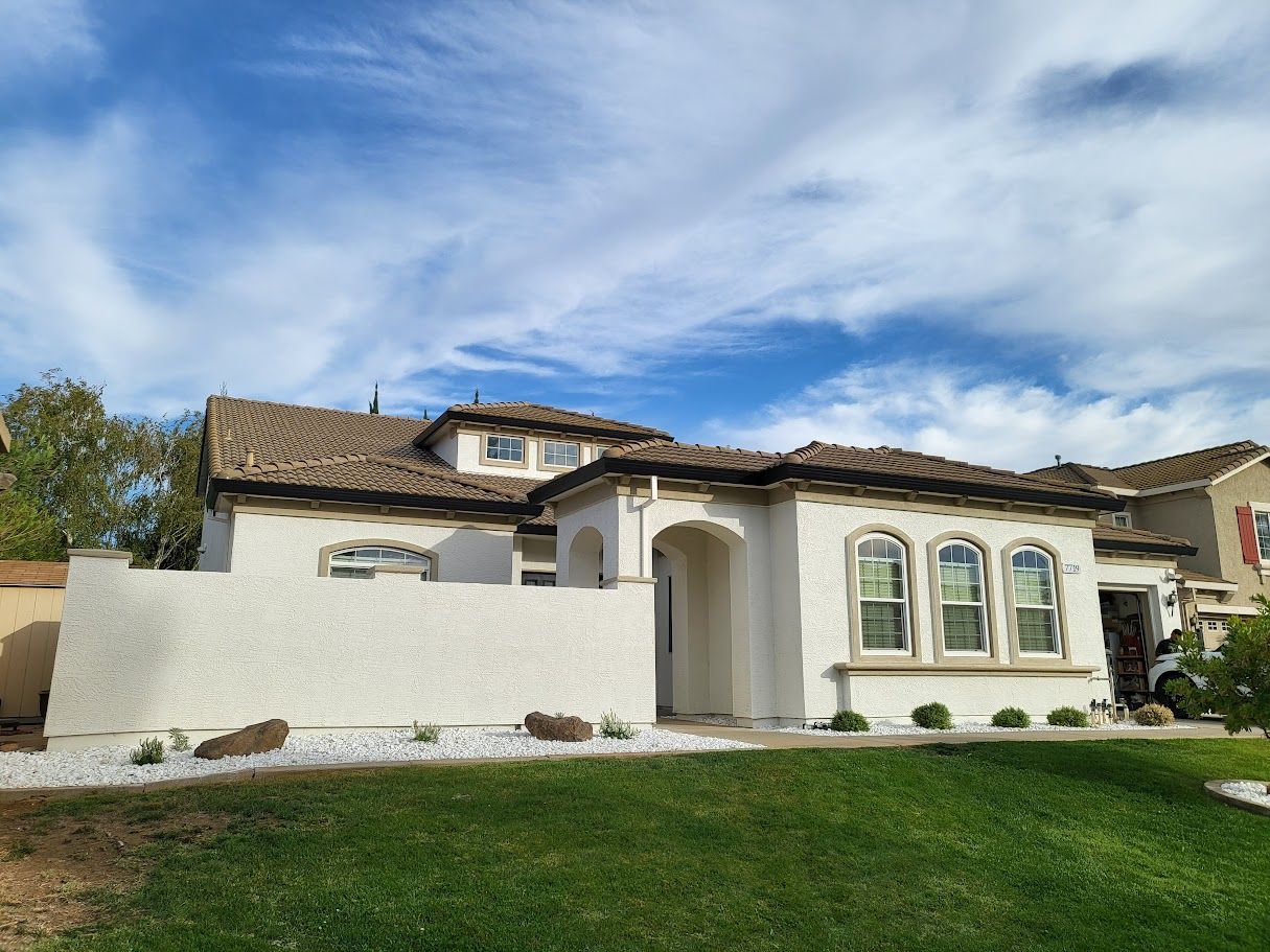 White stucco house with brown tile roof, arched windows, and green lawn.