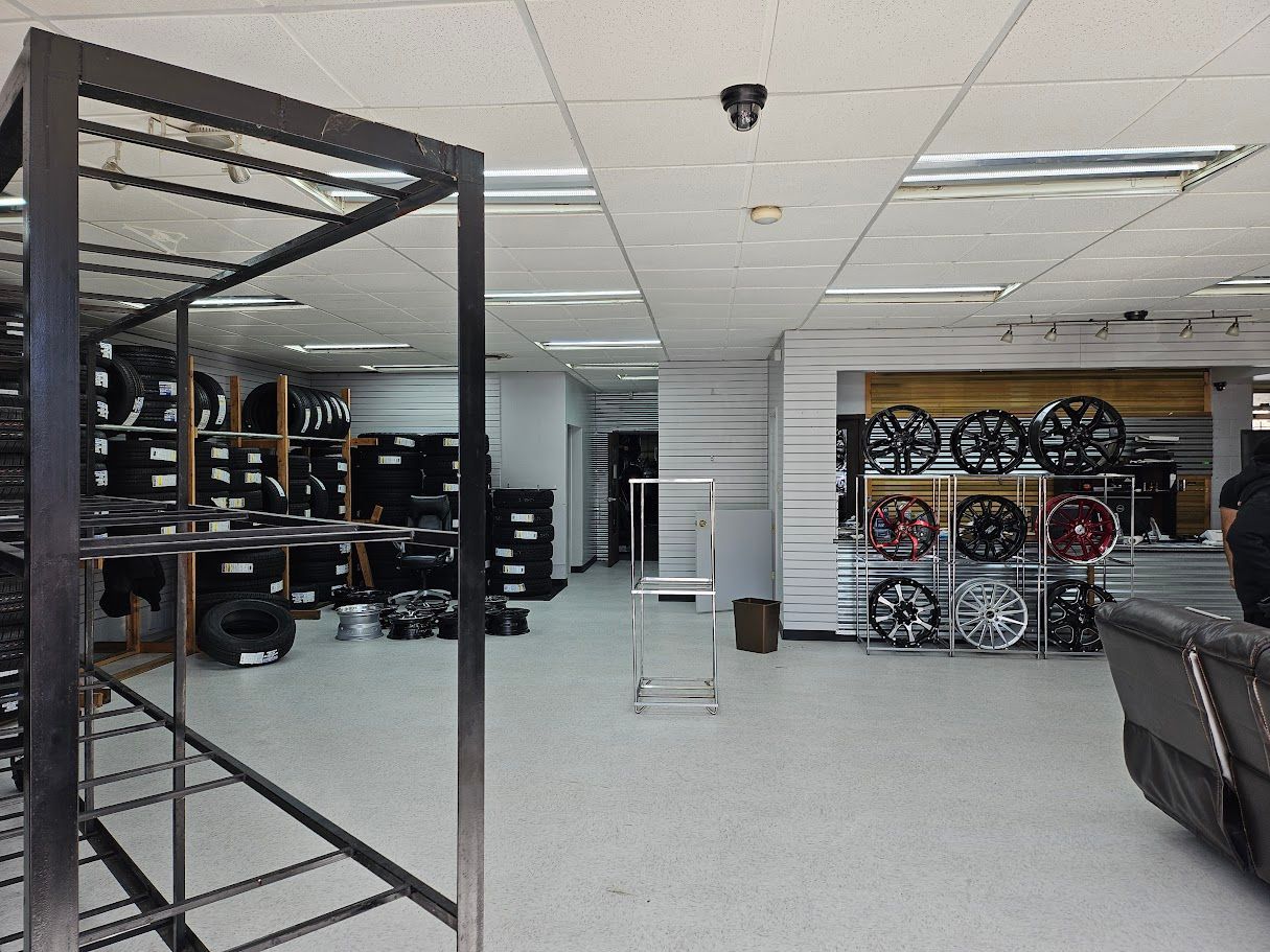 Inside a tire shop, display racks hold tires and wheels. A few customers are visible.