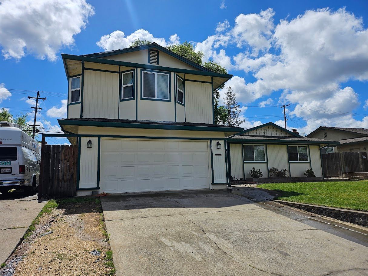 Two-story house with a white garage door, blue sky, and green trim. A driveway leads up to the house.