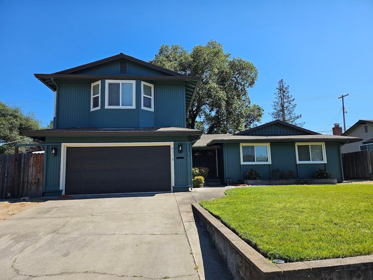 Two-story teal house with attached garage, single-story side, and green lawn against a bright blue sky.