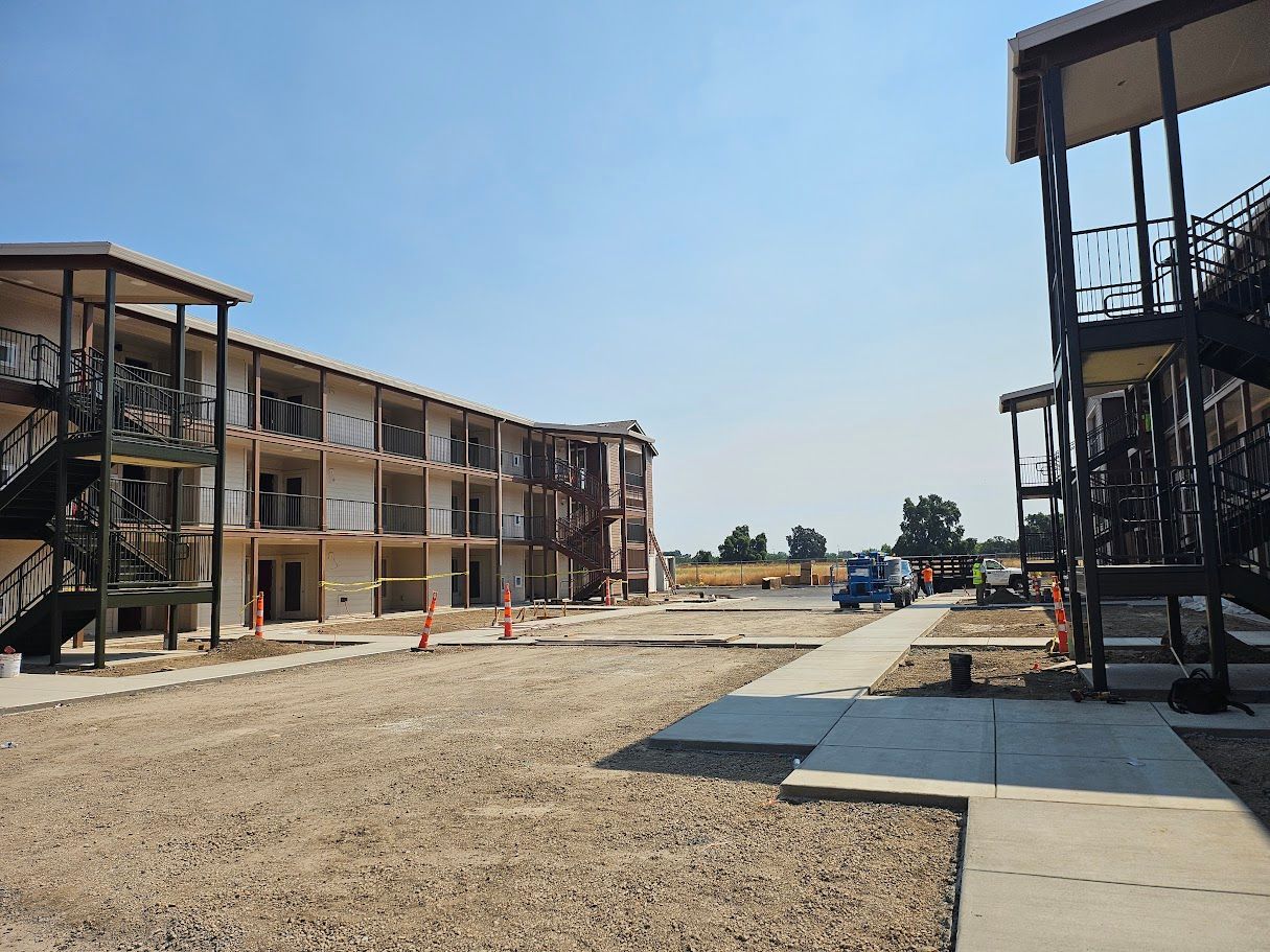 Apartment buildings under construction. Exterior view with unfinished walls, gravel ground, and blue sky.