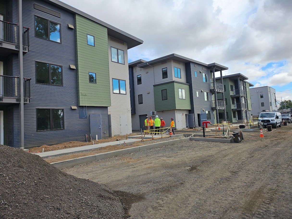 Buildings under construction, crews working, gravel road, blue, green, and gray siding.