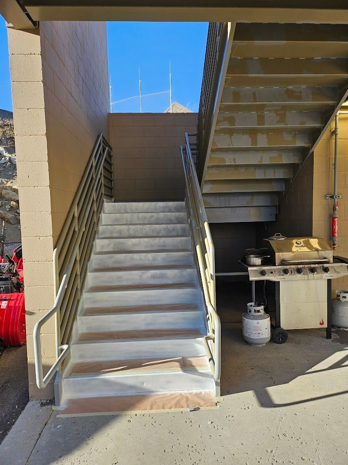 Exterior staircase with metal railings, leading upwards. Grill and propane tanks visible below.