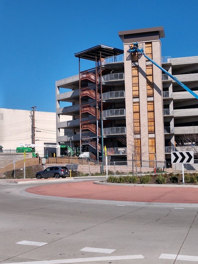 Construction site: parking garage under construction, workers in lift, staircase. Sunny day.